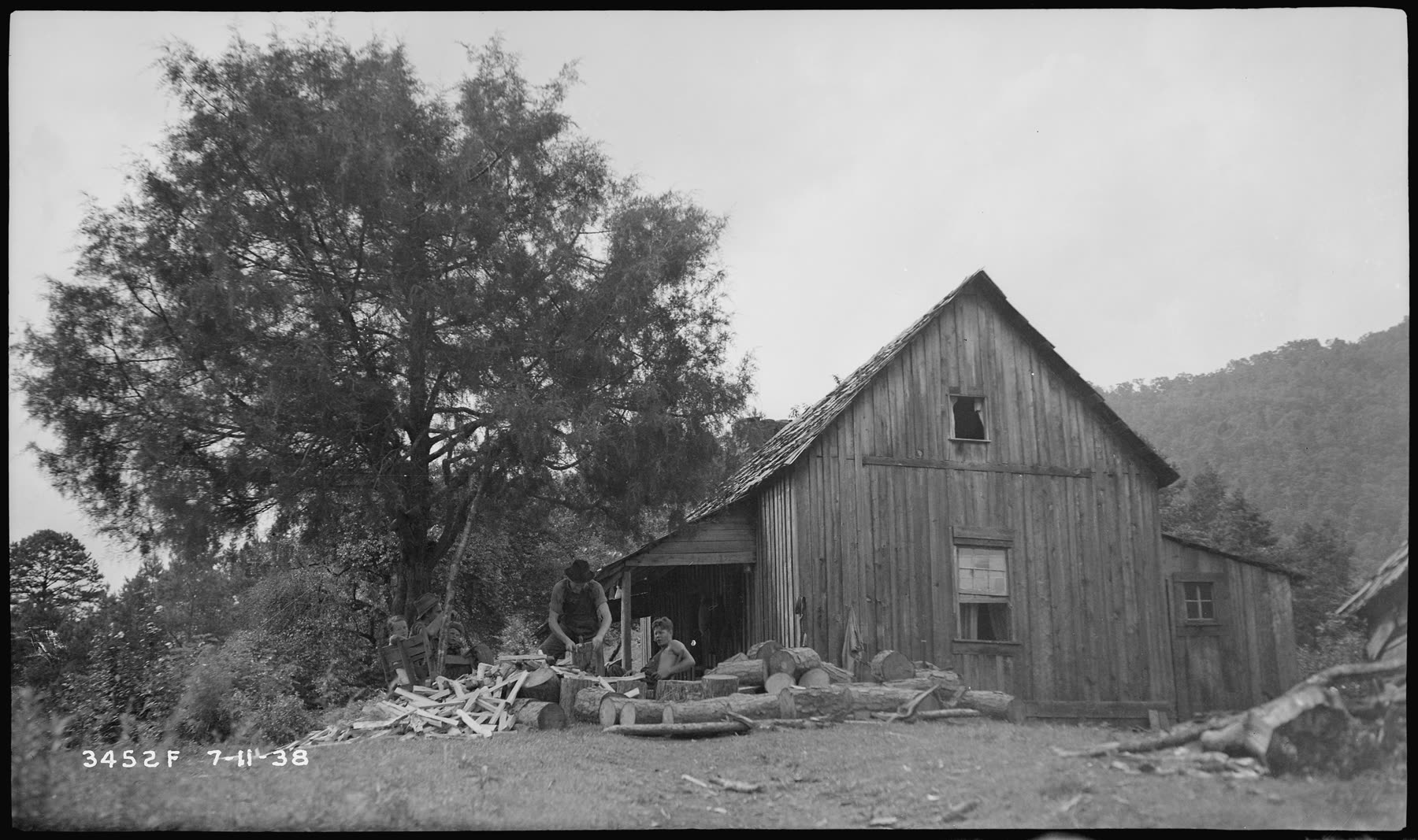 Dillard Morrow's log house with men splitting wood beside a large tree