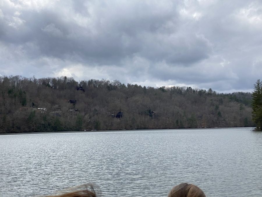 Calm lake under a cloudy sky, with tree-covered hills across the water