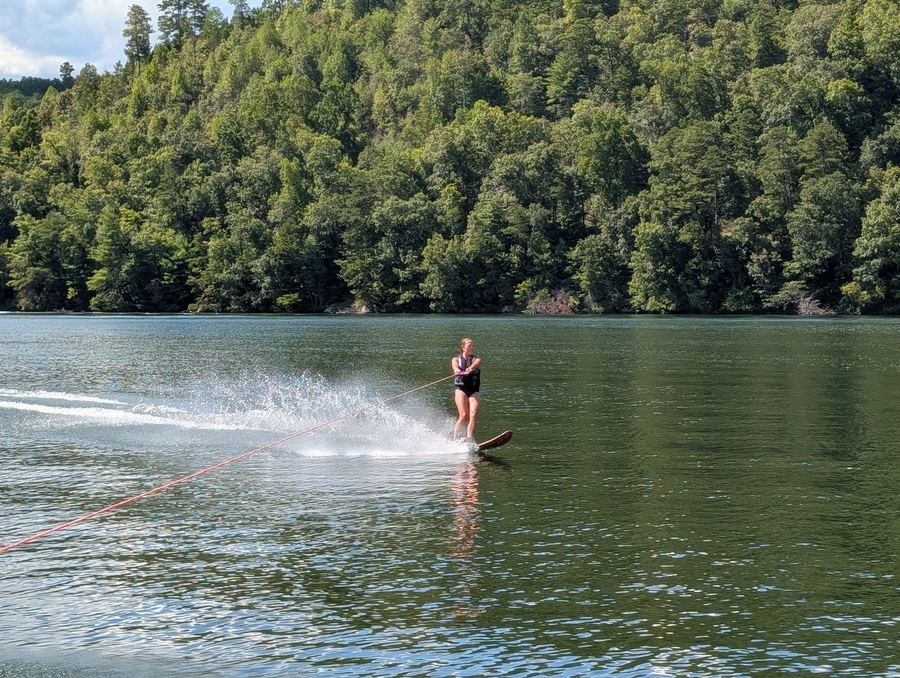 A waterskier behind a spray of water on the lake, with forested hills behind
